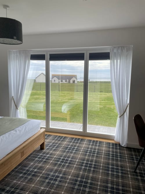 Modern bedroom at Flotnar Hus with sea view through large glass doors overlooking green fields and coastal landscape in