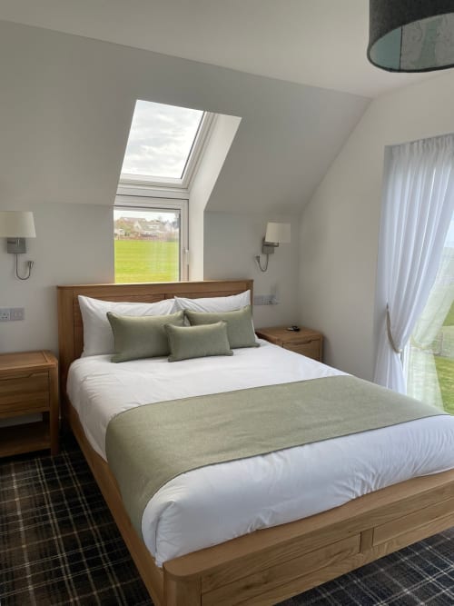 Modern bedroom at Flotnar Hus with wooden bed, sea view through skylight, green pillows, and garden views in Keiss
