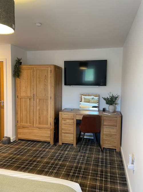 Flotnar Hus Room 2 in Keiss with wooden wardrobe, desk, brown chair, flat-screen TV, and plaid carpet