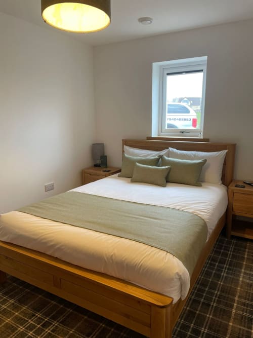 Modern bedroom at Flotnar Hus B&B in Keiss with wooden bed, olive green linens, and window overlooking countryside