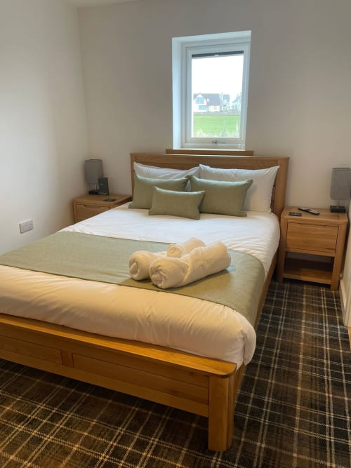 Bright bedroom at Flotnar Hus B&B in Keiss with wooden bed, white bedding, green cushions, rolled towels, and rural view from