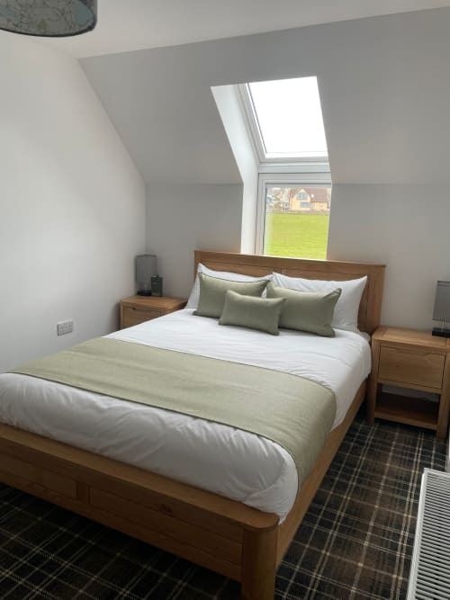 Bright bedroom at Flotnar Hus B&B in Keiss with wooden bed, green bedding, skylight window overlooking green fields, and
