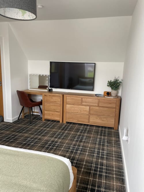 Modern hotel room with wooden desk, flat-screen TV, makeup mirror, and burgundy chair at Flotnar Hus B&B