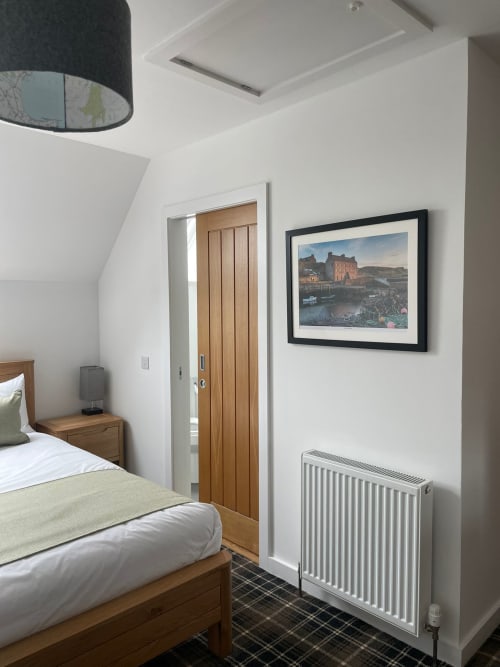 Modern bedroom at Flotnar Hus in Keiss with wooden bed, white walls, radiator, and framed coastal artwork above desk