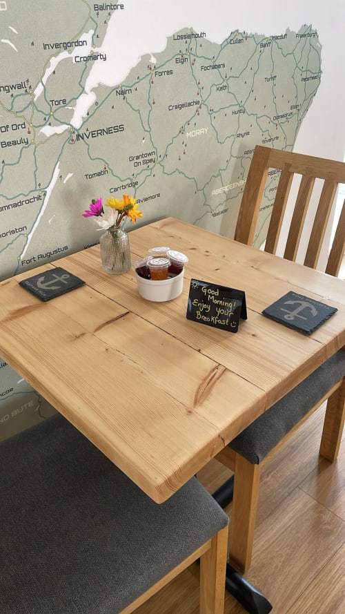 Wooden dining table with breakfast items and flowers, map of Scottish Highlands on wall at Flotnar Hus B&B in Keiss