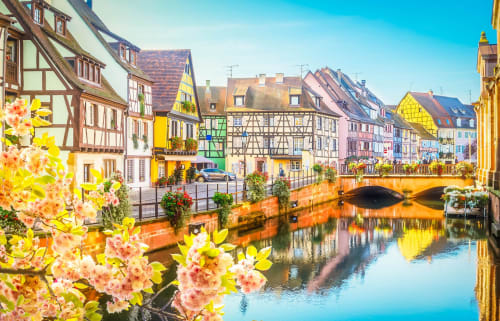 Des maisons à colombages charmantes et fleurs roses encadrent un pont de canal à Dambach la Ville, France, accueil du Petit Havre de