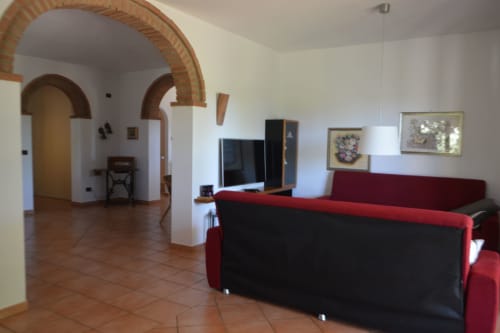 Soggiorno moderno con divano rosso e nero, TV a schermo piatto e arco in mattoni nell'appartamento Villa Collebelvedere a Fara
