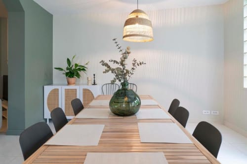 Modern dining room at Château Le Conte with wooden table, black chairs, green glass vase, and woven pendant light above