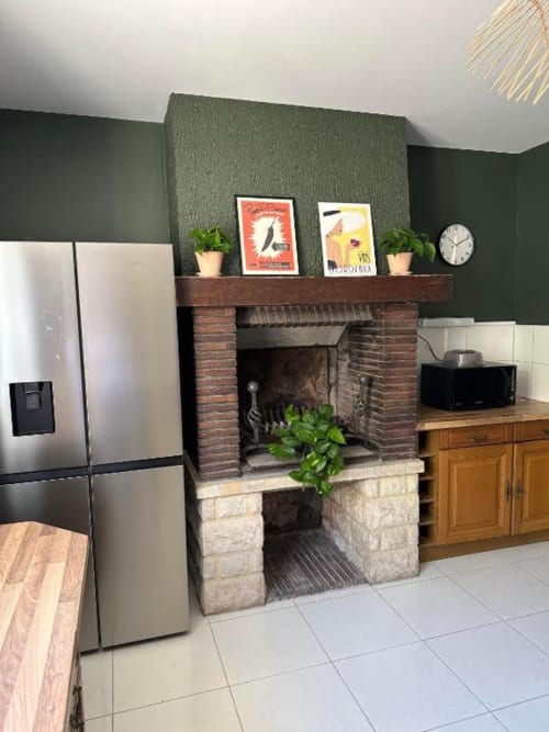 Modern kitchen with brick fireplace, stainless steel fridge, wooden cabinets, and green accent wall at Château Le Conte gîte
