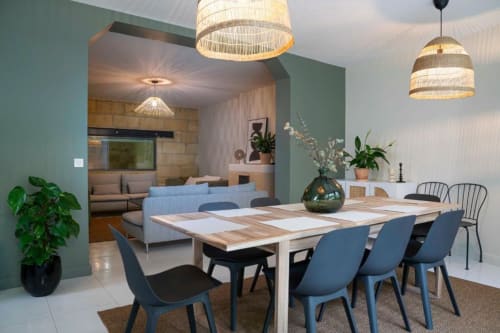 Modern dining room at Château Le Conte Saint-Emilion with wooden table, blue chairs, pendant lights, and garden view through