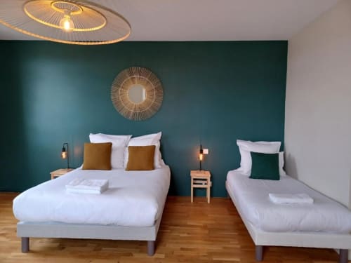 Modern bedroom at Château Le Conte with teal accent wall, two beds with white linens, golden accents, wooden floor, and