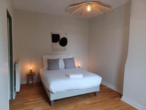 Modern bedroom with white bed, gray pillows, wooden floor, decorative wall art, and woven ceiling light at Château Le Conte