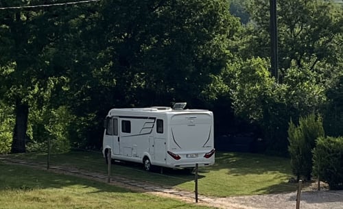 Witte camper geparkeerd op grasveld omgeven door bomen bij Maison d'hôtes de La Boissière in Andillac
