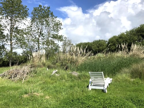 White lounge chair on green lawn overlooking reeds and trees at Le Lama Zébré in Penmarch