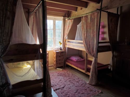 Charming bedroom at Le Lama Zébré in Penmarch with multiple canopy beds, sheer curtains, and rustic wooden beams