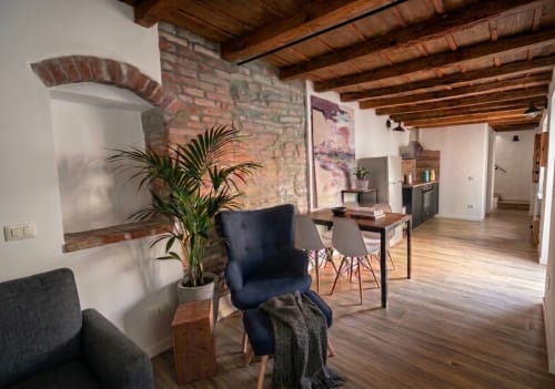 Modernes Loft-Apartment in Bergamo mit Backsteinwänden, Holzbalken, Esstisch, blauem Stuhl, Topfpflanze und offenem Grundriss