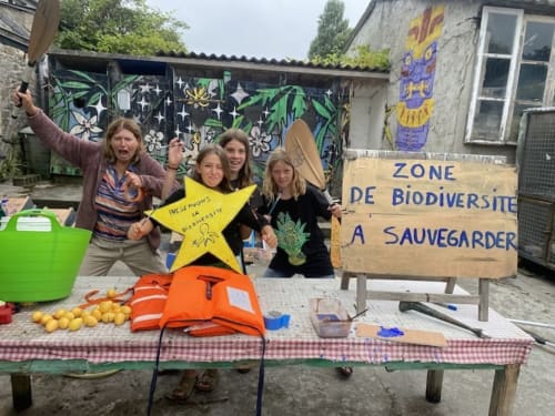 Four women at Le Lama Zébré eco-guesthouse in Penmarch display biodiversity conservation sign and yellow star craft