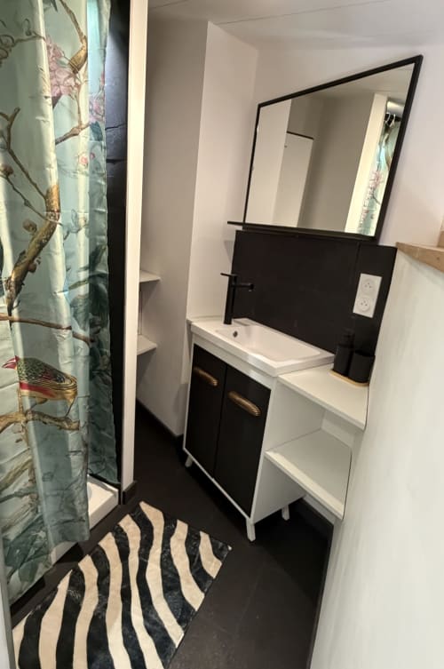 Modernes Badezimmer des Ferienstudios „Occitan Heritage“ in La Sarrasine in Aiguèze, 30760, flussabwärts der Gorges de l’Ardèche gelegen, mit schwarz-weißem Waschbeckenmöbel, Spiegel und Dusche.
