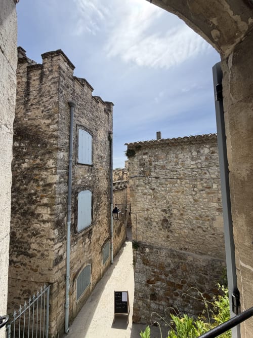 Blick aus dem Fenster des Ferienstudios „Occitan Heritage“ in La Sarrasine auf die historische gepflasterte Gasse von Aiguèze mit mittelalterlichem Turm, Kulturerbe nahe der Gorges de l’Ardèche.
