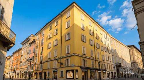 Le facciate gialle e corallo dell'hotel Palazzo Garibaldi a Parma con finestre scuri affacciano su una piazza soleggiata in Italia