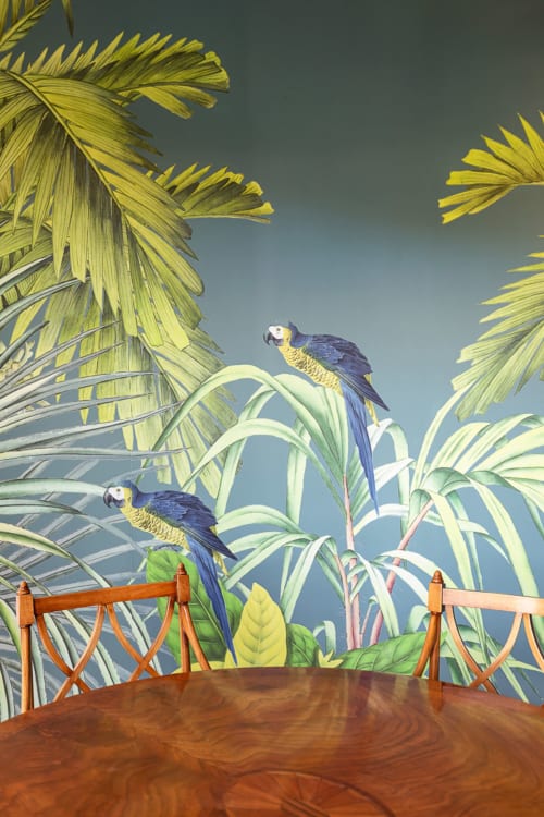 Tropical mural with blue parrots and palm fronds above wooden dining table at Terrestre Roma apartment in Rome