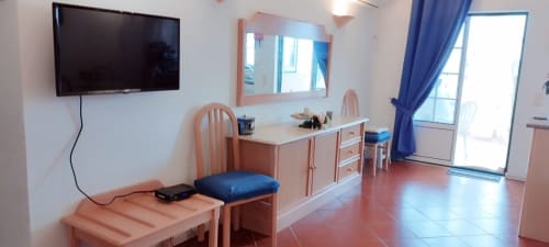 Quarto luminoso em Sweet Home Portimão com móveis de madeira, TV, escrivaninha, kitchenette e detalhes azuis