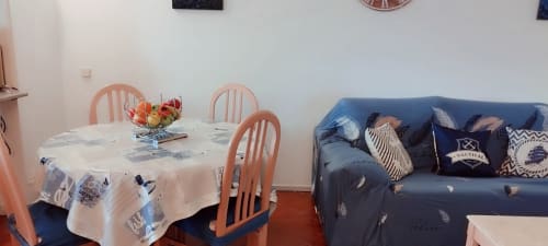 Sala de estar e jantar com mesa redonda, cadeiras coral, tigela de frutas e sofá azul com almofadas na propriedade de Portimão