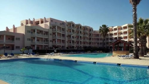 Área de piscina do Sweet Home Estrela do Vau em Portimão com piscinas turquesas, edifícios rosa e palmeiras