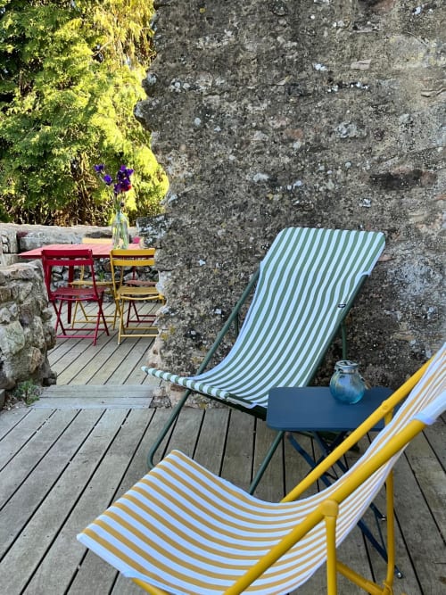 Chaises longues colorées sur la terrasse en bois de la Seigneurie du Bois Moreau, Durtal, avec mur de pierre et fleurs violettes