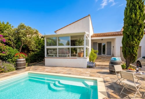 Villa Chez Mara à Canet-en-Roussillon avec piscine turquoise, transats et terrasse vitrée moderne donnant sur un jardin ensoleillé