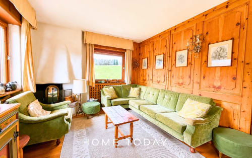 Cozy living room with green sofa, wooden pine walls, fireplace, and mountain views at Cortina d'Ampezzo apartment
