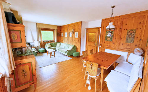 Spacious wooden alpine apartment in Cortina d'Ampezzo with dining table, green sofa, and mountain views