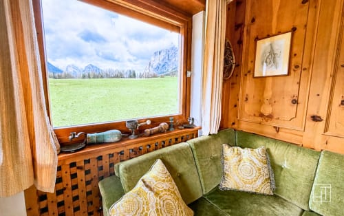 Cozy wooden alpine apartment with green sofa, mountain view window overlooking Cortina d'Ampezzo valley and peaks