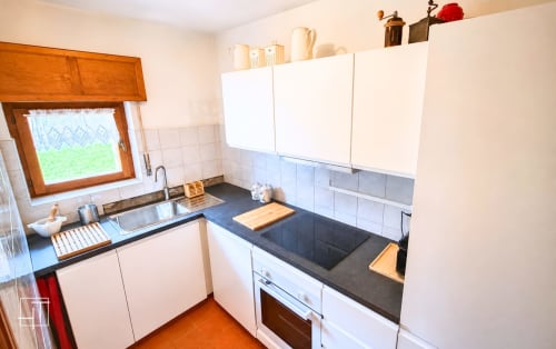Modern kitchen in Cortina d'Ampezzo apartment with white cabinets, dark countertops, stove, and mountain view window