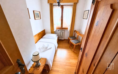 Cozy bedroom in Cortina d'Ampezzo apartment with wooden furnishings, white bedding, and mountain views