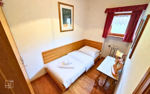 Cozy bedroom in Cortina d'Ampezzo apartment with wooden bed, white linens, mountain view window, and hardwood floors