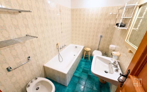 Bathroom with white bathtub, dual sinks, toilet, and teal floor tiles in Cortina d'Ampezzo apartment