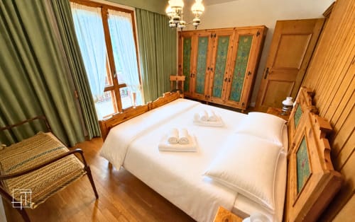 Spacious wooden bedroom in Cortina d'Ampezzo apartment with queen bed, wardrobe, mountain views, and green curtains