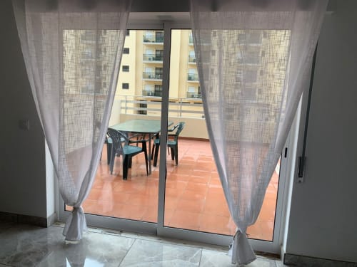 Varanda de apartamento com portas de vidro, cortinas translúcidas, mesa e cadeiras de jantar com vista para a cidade de Portimão