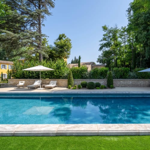 Luxury pool at Le Domaine du Fortin in Ménerbes with lounge chairs, umbrella, and manicured gardens