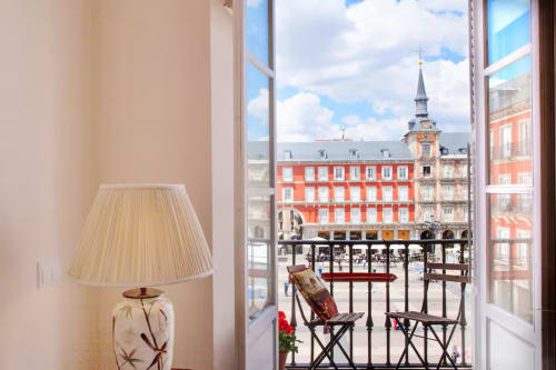 Balcony view of Madrid's Plaza Mayor from a charming apartment, featuring red colonial buildings and a cream-colored lamp