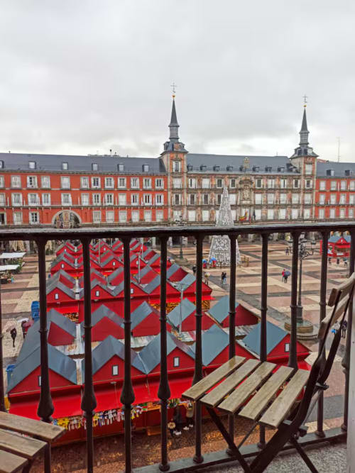 View from balcony of Madrid's Plaza Mayor with red market stalls and historic red buildings with church spires
