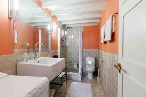 Modern bathroom with orange and white walls, double sink, shower, and toilet in Madrid apartment