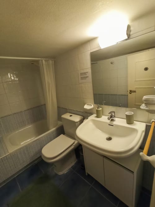 Modern bathroom in Madrid apartment with white tiles, sink, toilet, shower, and mirror lighting