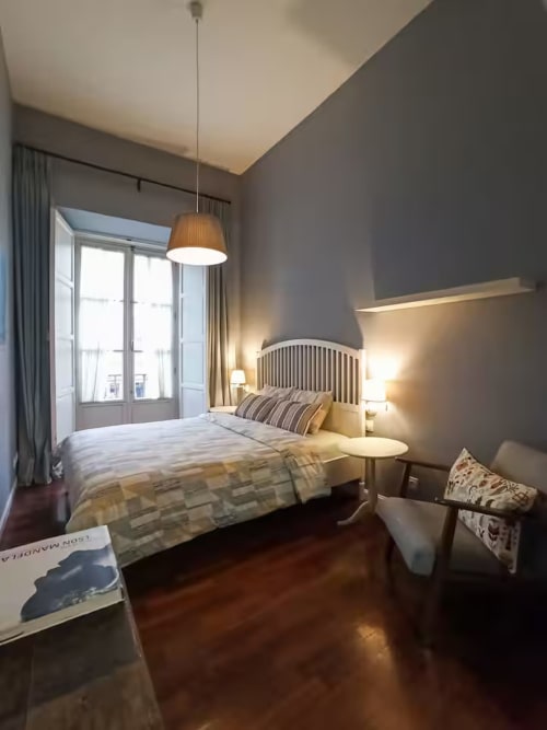 Modern bedroom in Madrid apartment with city view balcony, hardwood floors, pendant lighting, and striped bedding