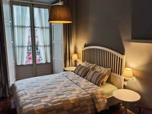 Elegant bedroom in Madrid's Plaza Mayor apartment with queen bed, warm lighting, balcony doors, and city views