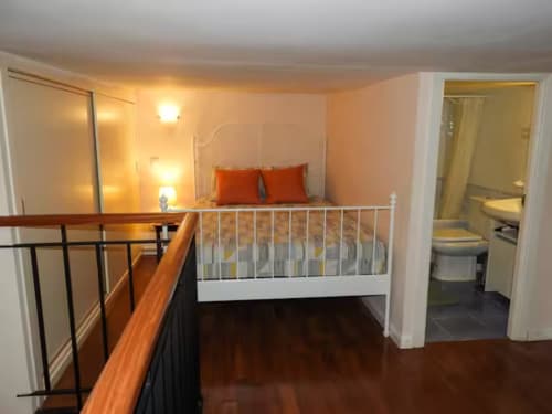 Loft bedroom in Madrid apartment with white crib, orange bedding, hardwood floors, and en-suite bathroom access.