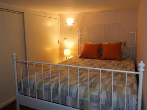 Warm bedroom with white metal bed, red pillows, hardwood floors, and ambient lighting at Charming View Plaza Mayor, Madrid