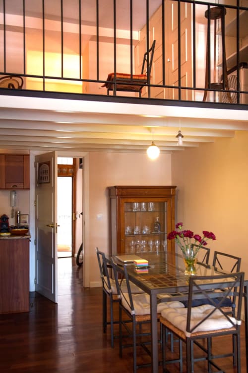 Modern apartment dining area with city views, featuring wooden table, mezzanine level, and kitchen in Madrid
