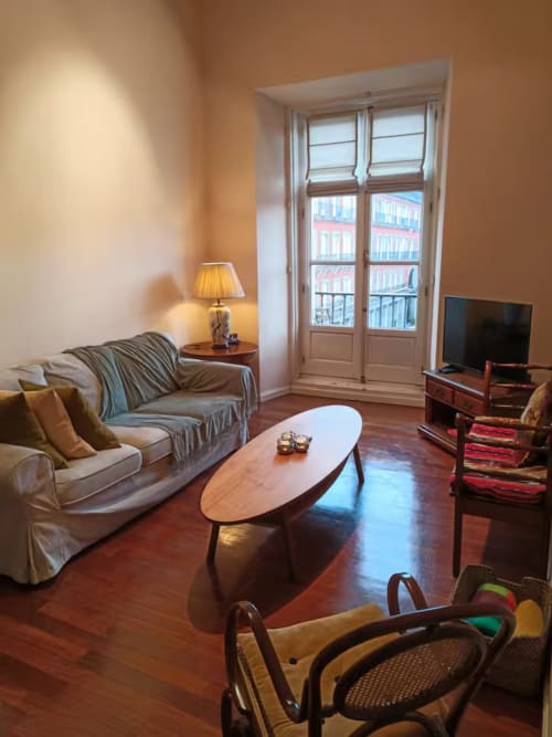 Elegant Madrid apartment living room with hardwood floors, city view balcony, sofa, TV, wooden coffee table, and lamp